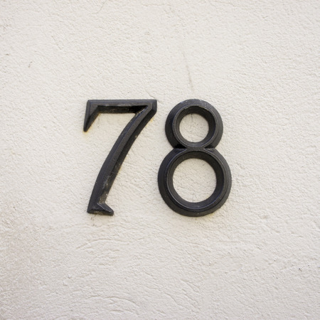 metal house number seventy eight. two separate numerals on a white stucco wall.の写真素材
