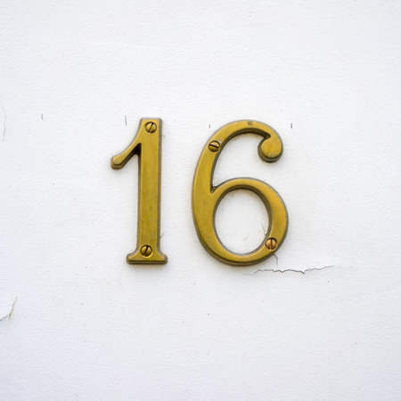 bronze house number sixteen. Two separate numerals on a flaking wall