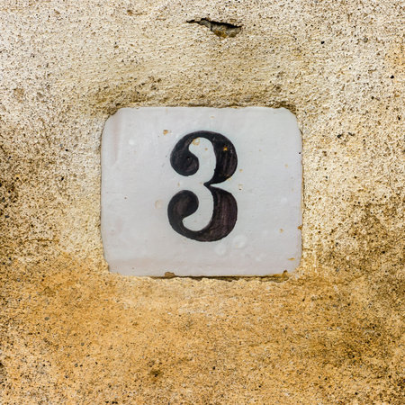 Ceramic house number three on a plastered wall
