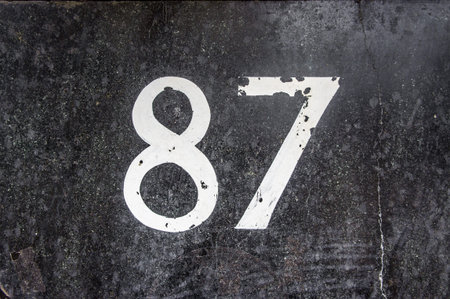 Hand painted house number eighty seven (87) on a stone wall