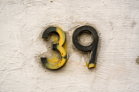 Bronze house number thirty nine on a white plastered wall. Partially sprayed over by yellow paint.の写真素材