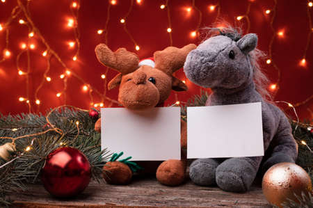 Cute reindeer in santa hat and horse toys holding a white writeable card, sheet of paper in a Christmas scenario.の写真素材