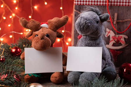 Cute reindeer in santa hat and horse toys holding a white writeable card, sheet of paper in a Christmas scenario.の写真素材