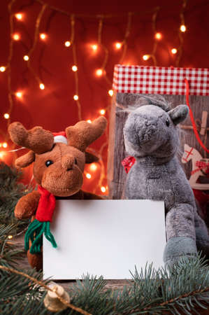 Cute reindeer in santa hat and horse toys holding a white writeable card, sheet of paper in a Christmas scenario.の写真素材