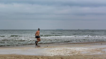 Sturdy sportsman warming up before submerging in freezing water on baltic beach. Gdansk, Poland, 12/02/2017のeditorial素材