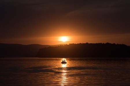Silhouette of fisher and dog sitting in boatの写真素材
