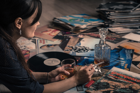 RUSSIA. Portrait of a beautiful girl, glass of whiskey, listening to music from vinyl LP records vintage.のeditorial素材
