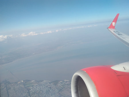 Wing of an airplane flying above the city in the blue sky.