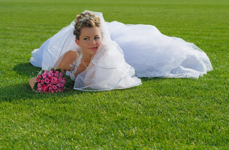 Young beautiful bride with flowers lying on the green grassの写真素材