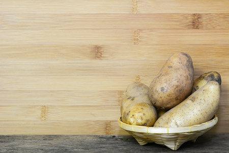 Potatoes in bamboo basket on wooden backgroundの写真素材