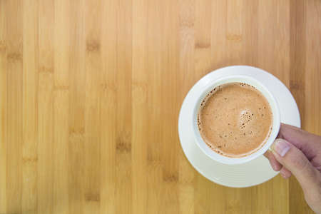 hand holding a coffee mug with wooden table backgroundの写真素材