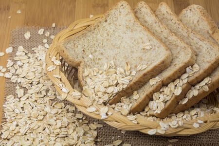 Whole wheat bread slices in basket with oats on tableの写真素材