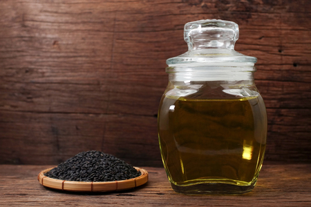 Black sesame oil in glass jar and sesame seeds on wooden tableの写真素材