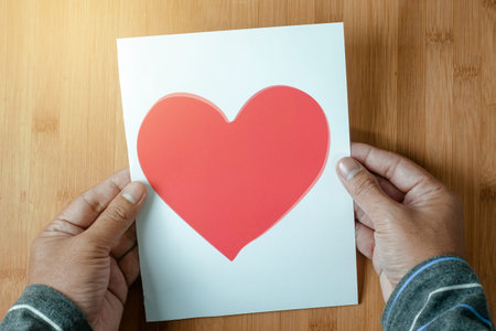 Two hand of man holding a paper red heart on wooden table
