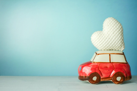 Miniature red car carrying a white heart on a cyan backgroundの写真素材