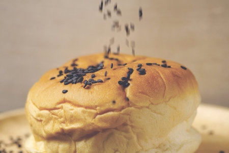 Black sesame seeds falling into burger bun