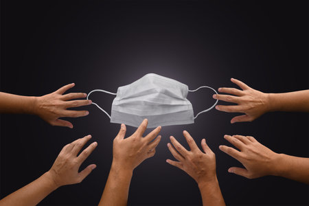 Mask with many hands try to grab or capture, shortage or surging high demand of respiratory mask to protect from Coronavirus, health protection from covid19 concept, Mask and hand on dark backgroundの写真素材