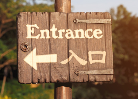 Bilingual wooden entrance signs with a white arrow to the left.の写真素材