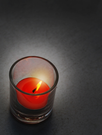 A red candle in a shot glass burning in dark background.の写真素材
