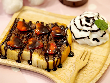 honey toast with slice strawberries and chocolate sauce on top and whip cream served on a wood board.の写真素材