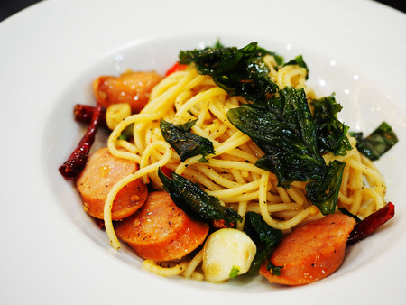smoked sausage spaghetti with garlic and fried basil served on a white plate.の写真素材