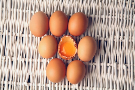 Broken egg surrounded by other eggs inside a basket の写真素材