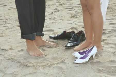 Couple feet treading the sand beach with their party shoesの写真素材