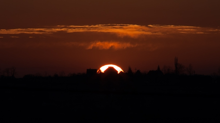 House Of The Falling Sun - Sunset behind distant house silhouette on horizon, burning orange color, flamelike clouds.の写真素材