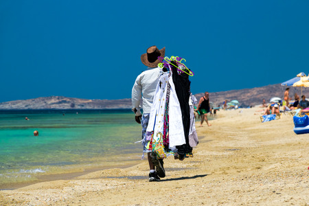 Seller on the beach / Back view of a man walking along the beach carrying clothes, Maragas (Plaka) beach, Naxos island, Cyclades, Greeceの写真素材