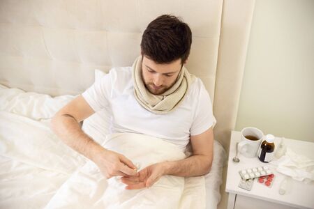 Man Taking Pills in Bed. Sick Man at Home Staying in Bed. Self Treatment Tabletsの写真素材