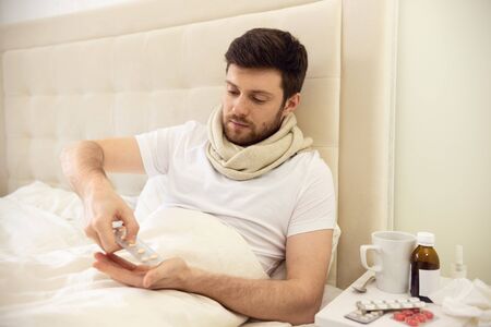 Man Taking Pills in Bed. Sick Man at Home Staying in Bed. Self Treatment Tabletsの写真素材