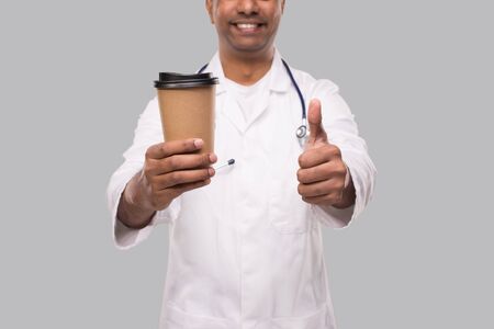 Man Doctor Holding Coffee Take Away Cup Smiling Close Up Isolated. Indian Doctor Holding Coffee To Go Cup. Isolatedの写真素材