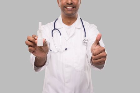 Doctor Holding Nose Spray Showing Thumb Up Close Up Isolated. Indian Man Doctor with Nasal Spray in Hands. Medicalの写真素材