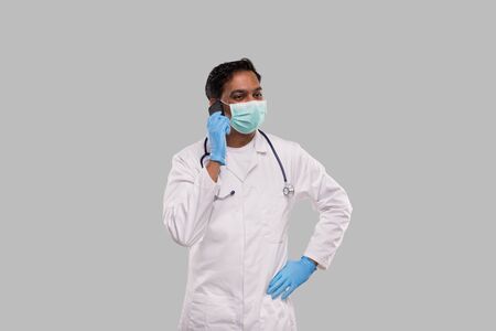 Doctor Talking on Phone Wearing Medical Mask and Gloves. Indian Man Doctor with Phone Isolatedの写真素材
