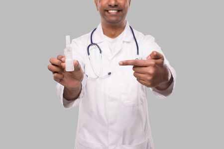 Doctor Pointing at Nose Spray Close Up Isolated. Indian Man Doctor with Nasal Spray in Hands Medicの写真素材