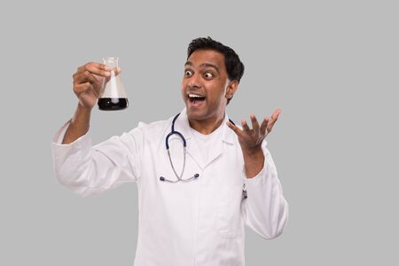 Male Doctor Excited Watching Flask with Colorfull Liquid Isolated. Science, Medical, Virus Concept. Indian Man Doctor Smilling.の写真素材