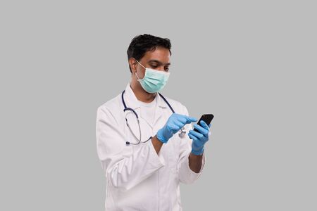 Doctor Chatting on Phone Wearing Medical Mask and Gloves. Indian Man Doctor with Phone Isolatedの写真素材