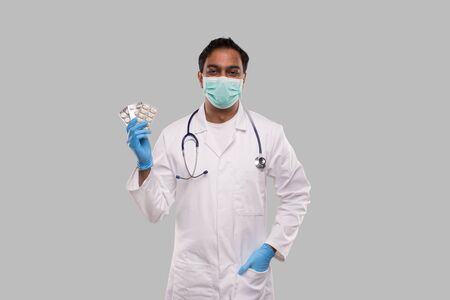 Man Doctor Showing Pills Wearing Medical Mask and Gloves. Doctor Holding Tablets. Indian Man Doctor Isolated.の写真素材