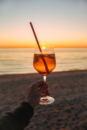 Girl Holding Glass of Drink on Beach at Beautyfull Romantic Sunset. Glass and Hand Close Up. Natureの写真素材