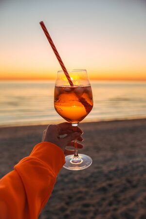 Girl Holding Glass of Drink on Beach at Beautyfull Romantic Sunset. Glass and Hand Close Up. Natureの写真素材