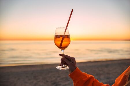 Girl Holding Glass of Drink on Beach at Beautyfull Romantic Sunset. Glass and Hand Close Up. Natureの写真素材
