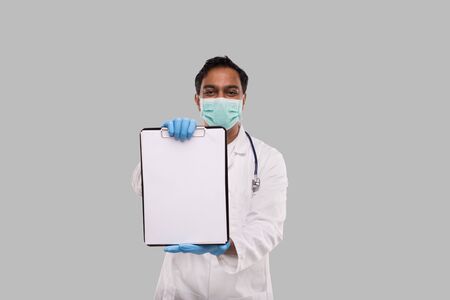 Doctor Showing Clipboard Wearing Medical Mask and Gloves Isolated. Indian Man Doctor Blank Clipboard in Handsの写真素材