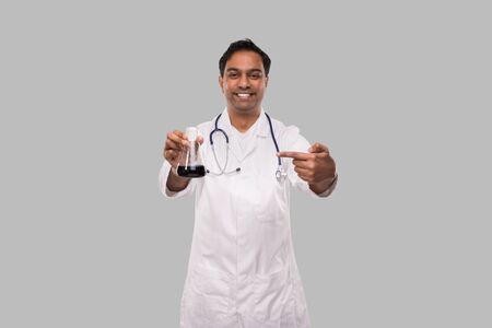 Male Doctor Pointing at Flask with Colorfull Liquid Isolated. Science, Medical, Virus Concept. Indian Man Doctor Smilling.の写真素材
