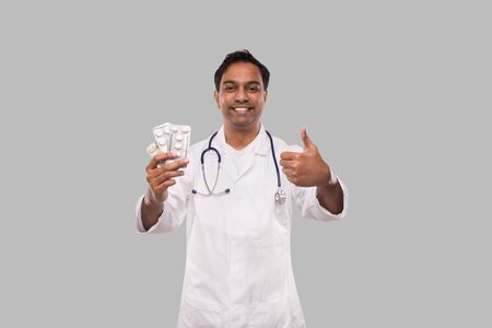 Man Doctor Showing Pills and Thumb Up. Doctor Holding Tablets. Indian Man Doctor Isolated.の写真素材