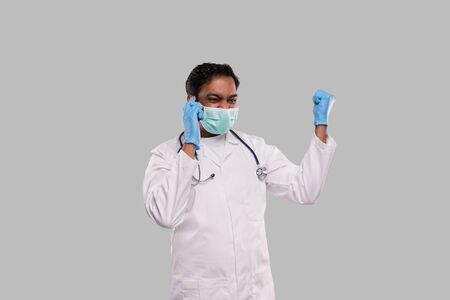 Doctor Talking on Phone Excited, Wearing Medical Mask and Gloves. Indian Man Doctor with Phone Isolatedの写真素材