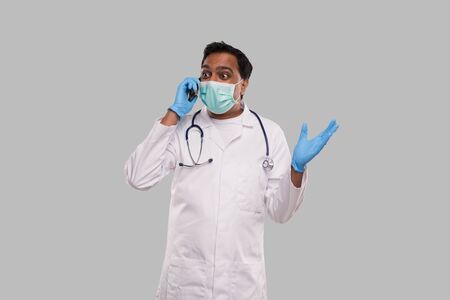 Doctor Talking on Phone Excited, Wearing Medical Mask and Gloves. Indian Man Doctor with Phone Isolatedの写真素材