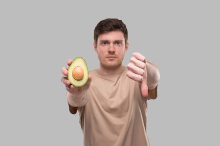 Man Showing Avocado and Thumb Down Close Up Isolated. Avocado Cut in Half. No Avocado, Stop Avocado Conceptの写真素材