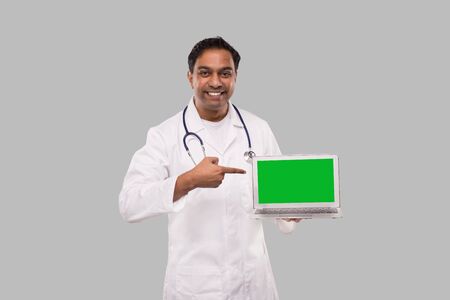 Doctor Pointing at Laptop Green Screen Watching in Camera Isolated. Male Indian Doctor with Laptop in Hands.の写真素材