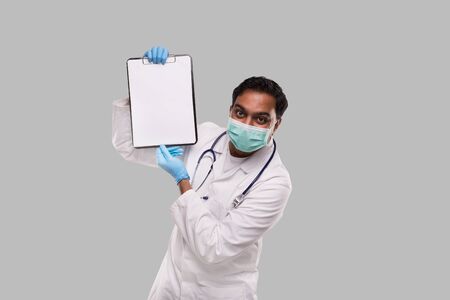 Doctor Showing Clipboard Wearing Medical Mask and Gloves Isolated. Indian Man Doctor Blank Clipboard in Handsの写真素材