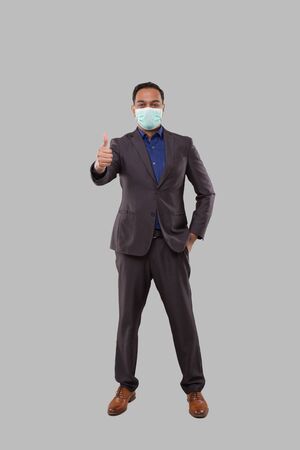 Businessman Wearing Medical Mask Showing Thumb Up Isolated. Indian Businessman Standing Full Lengthの写真素材
